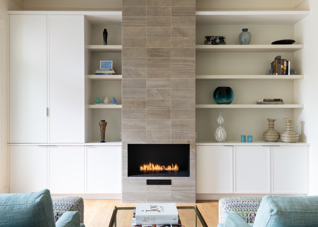 Clean minimalist fireplace wall with built in cabinets and simple decor in a remodeled living room by BBA Construction in Park City Utah